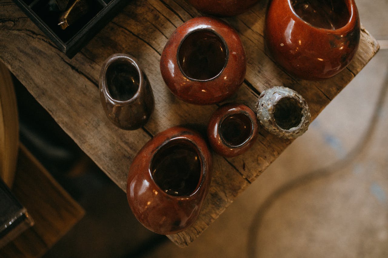 services-04 A collection of handmade ceramic pots with rich brown glaze on a rustic wooden table.